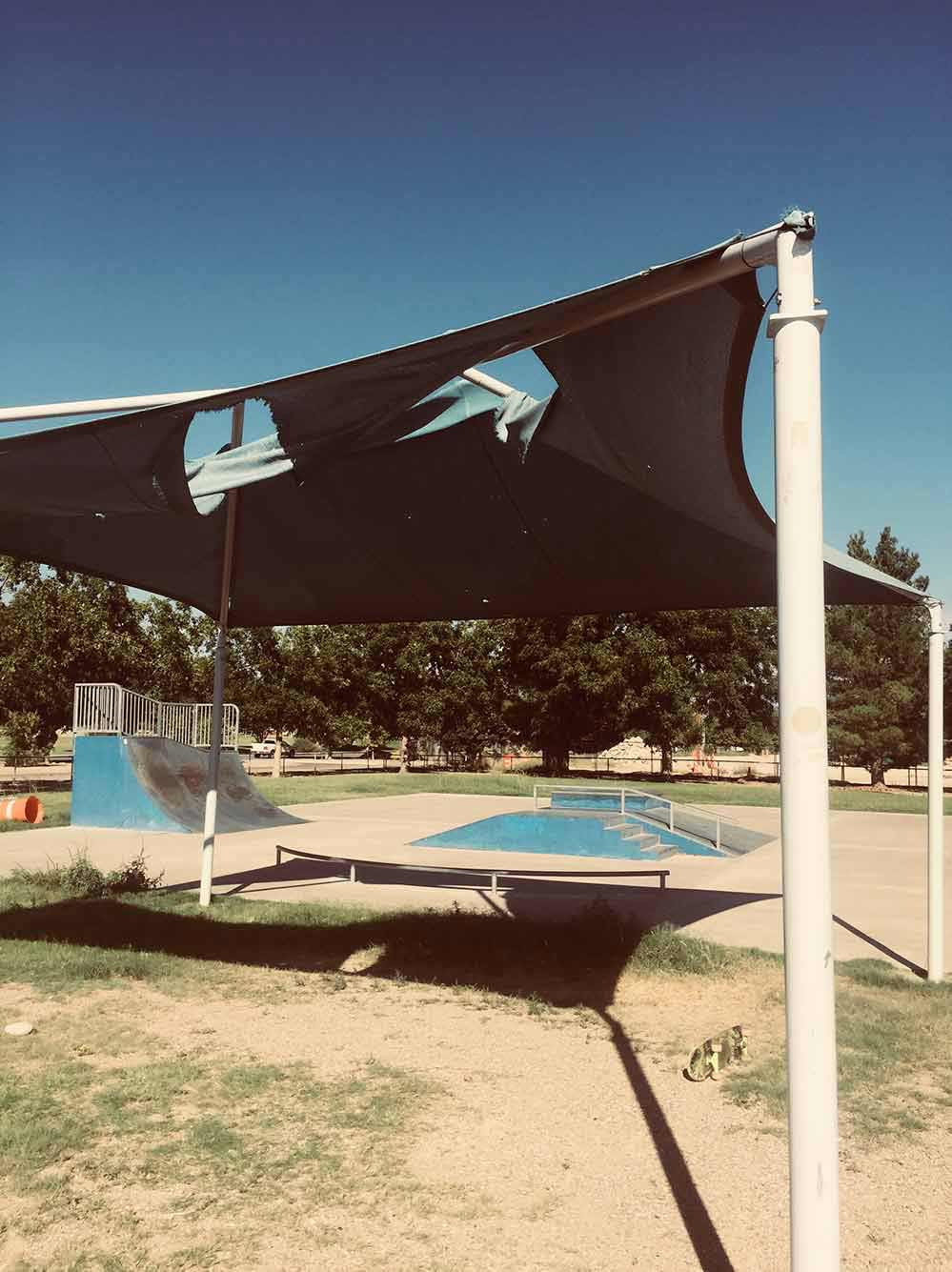 A canvas awning filled with holes over a dirt patch